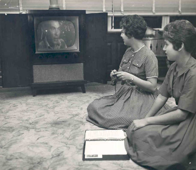 Two students sit on the floor to watch television in the recreation room of their dormitory