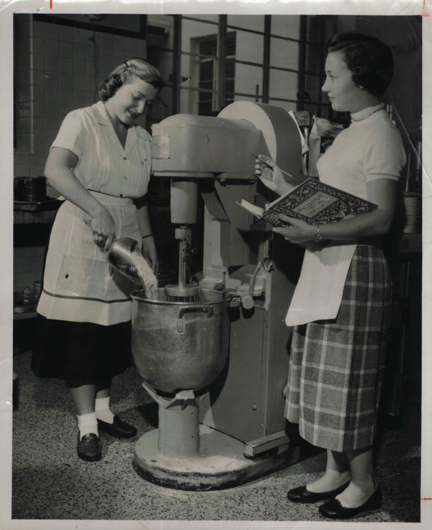 Student uses an industrial food mixer while another records cost and sales for Home Economics project