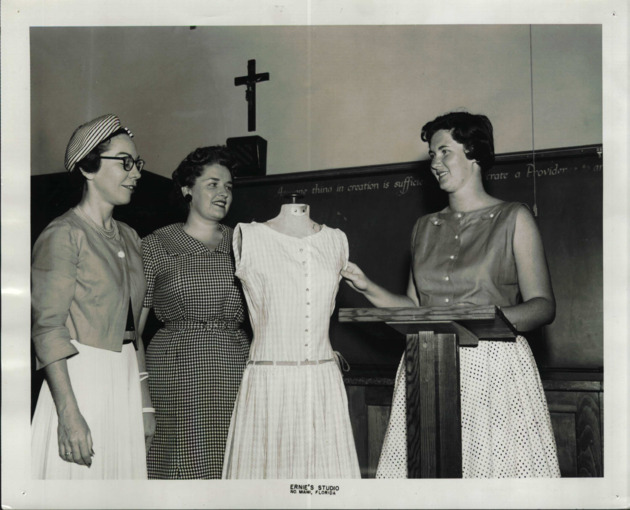 Students look over a dress on a sewing mannequin