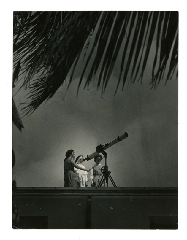 Two students assist a Dominican Sister in observing through telescope on Thompson Hall roof
